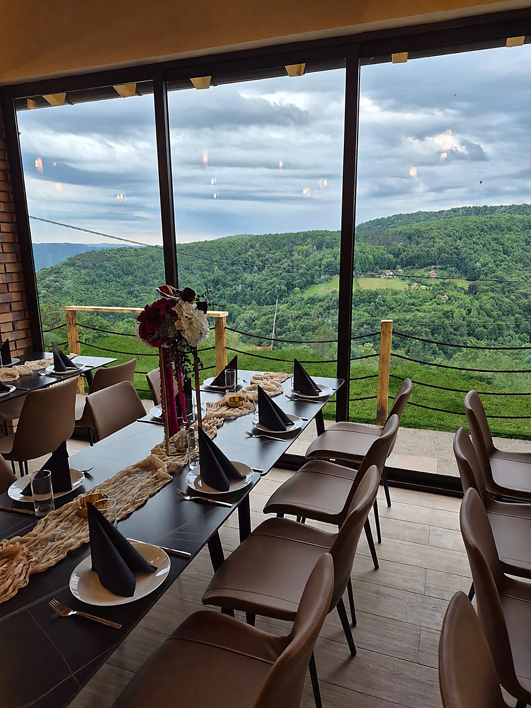 Svečano postavljen sto uz panoramski prozor sa pogledom na brežuljke